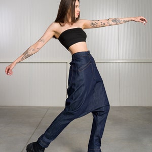K&ouml;nnte beinhalten: Eine Frau tr&auml;gt ein schwarzes Bandeau-Top und eine dunkelblaue Jeanshose mit einem einzigartigen, weiten Stil. Sie tr&auml;gt schwarze Sneaker mit einer dicken Sohle.