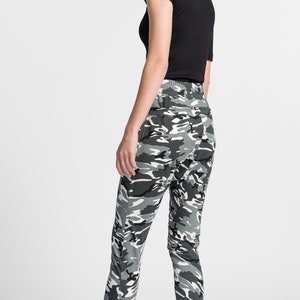 May include: A person wearing black and gray camouflage pants with a black t-shirt and black and green high-top sneakers.