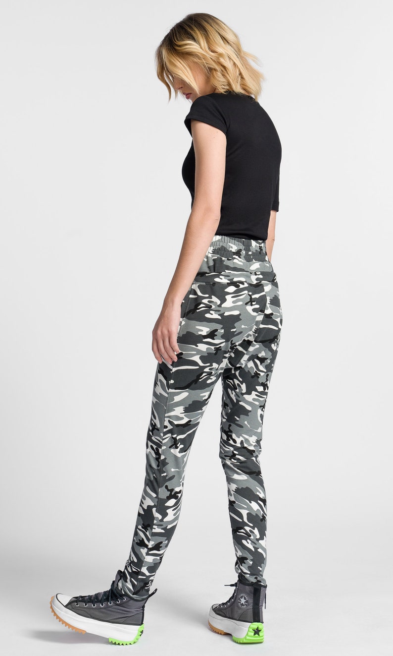 May include: A person wearing black and gray camouflage pants with a black t-shirt and black and green high-top sneakers.