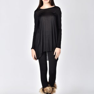 Op de afbeelding: Een persoon draagt een zwarte tuniek met lange mouwen en een zwarte legging. De tuniek heeft een asymmetrische zoom. Ze draagt zwarte laarzen met bontafwerking. De achtergrond is effen wit.