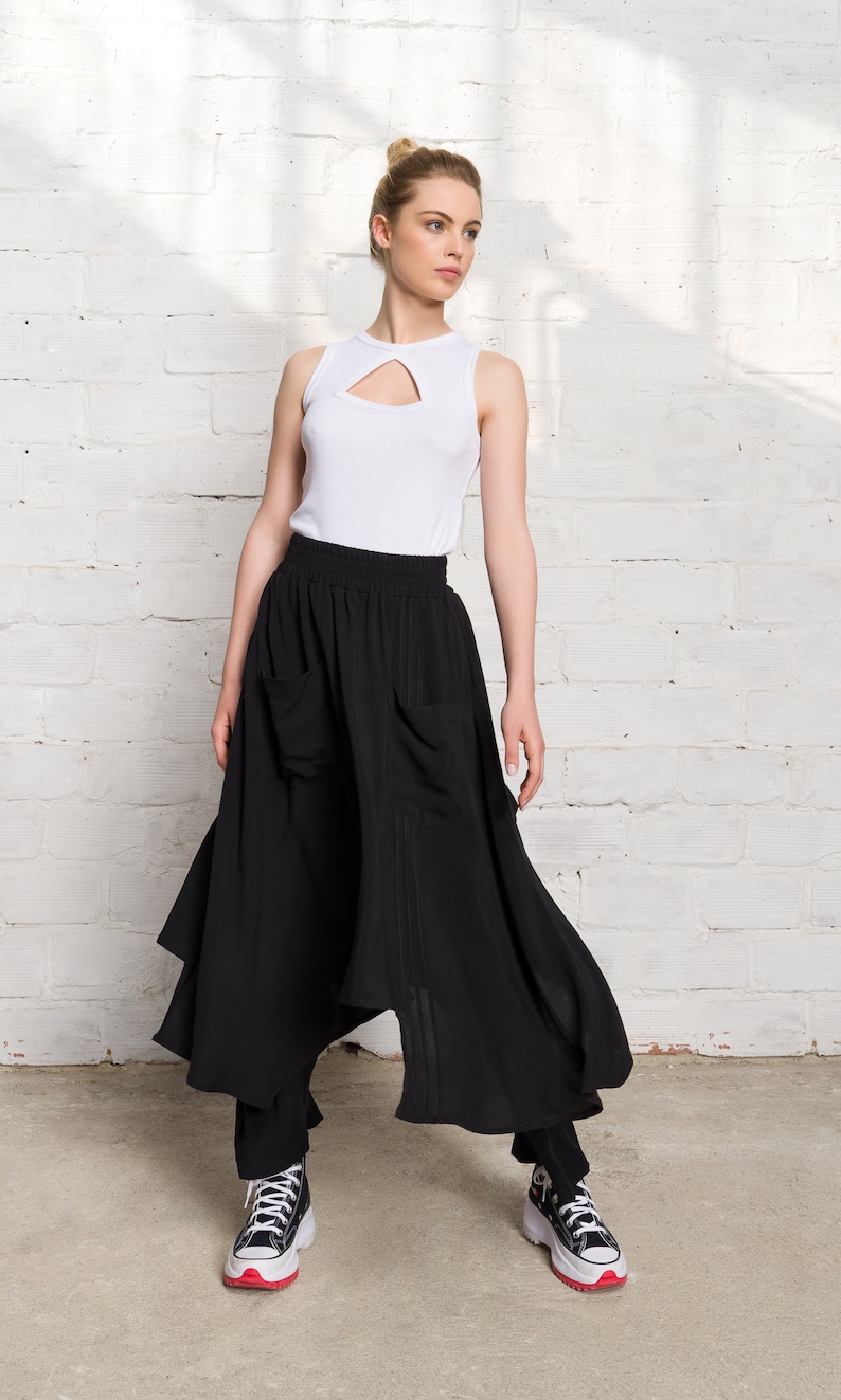 Pode incluir: Uma mulher vestindo um top branco sem mangas com um decote de chave e uma saia preta assim&eacute;trica com bolsos. Ela est&aacute; usando t&ecirc;nis preto e branco com detalhes vermelhos.