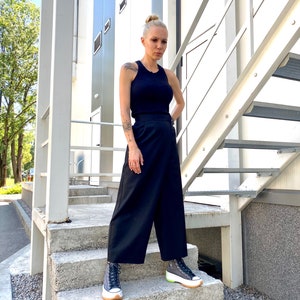 May include: A woman wearing a black tank top and black wide-leg pants. She is standing on a set of stairs and wearing black and white platform sneakers.