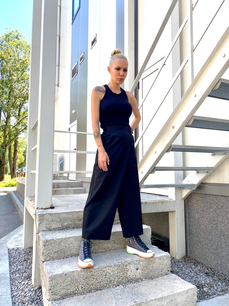 May include: A woman wearing a black tank top and black wide-leg pants. She is standing on a set of stairs and wearing black and white platform sneakers.
