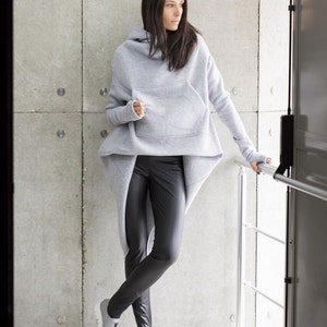 May include: A gray hooded sweatshirt with a long, asymmetrical hemline and a large pocket on the front. The sweatshirt is paired with black leggings and silver shoes.