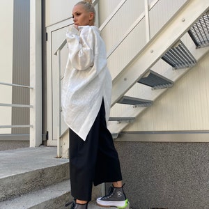 May include: A person wearing a white long-sleeve shirt and black pants. The person is wearing gray high-top sneakers with white soles and neon green accents. The sneakers have a star logo on the side. The person is standing on concrete steps next to a metal staircase.