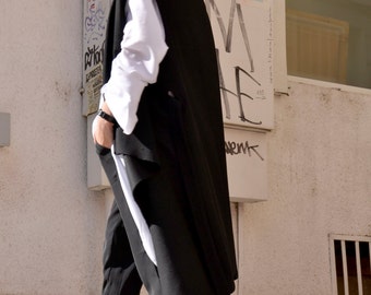 May include: A woman wearing a black sleeveless coat over a white shirt and black pants. She is wearing white sneakers with a heart pattern.