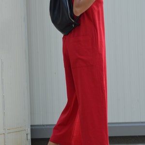 May include: A woman wearing a red sleeveless jumpsuit with a black leather backpack. She is wearing black sandals and walking on a sidewalk.