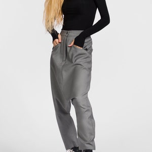 May include: A woman wearing a black long-sleeved shirt with a cut-out neckline and gray, loose-fitting pants. She is wearing black boots with white laces that say "Love" on them.
