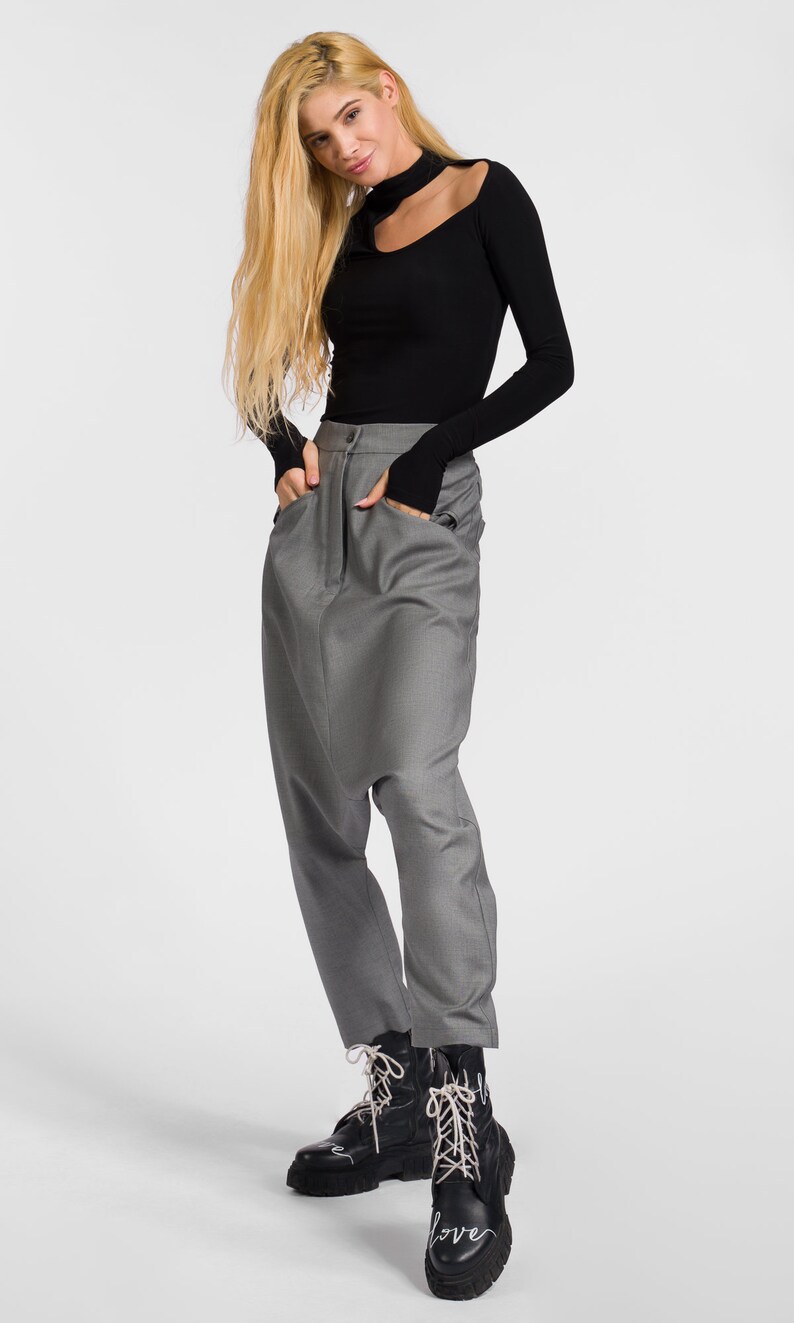 May include: A woman wearing a black long-sleeved shirt with a cut-out neckline and gray, loose-fitting pants. She is wearing black boots with white laces that say "Love" on them.