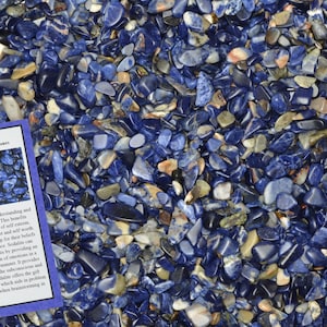 May include: A close-up image of a pile of small, blue sodalite stones. The stones are tumbled and have a variety of shapes and sizes. A small card with the text "Sodalite Home Decor / Healing Stones" is visible in the lower left corner of the image.