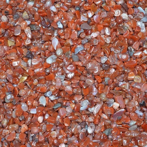 May include: A close-up view of a collection of polished, small, red-orange gemstones. The stones vary in size and shape, with a glossy, reflective surface. The overall effect is a rich, textured display of natural beauty.
