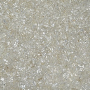 May include: A close-up view of a large quantity of small, clear quartz crystals. The crystals are scattered randomly and appear to be tumbled, giving them a smooth, rounded shape.