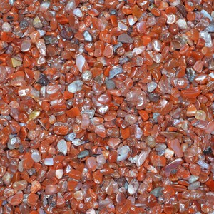 May include: A close-up view of a collection of small, red carnelian stones. The stones are smooth and polished, with a variety of shapes and sizes.