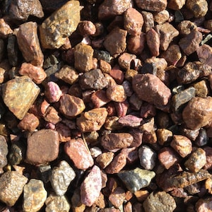 May include: A close-up of a pile of small, rough, red, brown, and gray stones. The stones are various shapes and sizes, and some have a shiny, metallic finish.