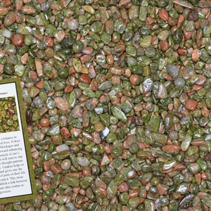 May include: A close-up image of a pile of small, smooth, polished green and red Unakite stones. The stones are tumbled and have a variety of shapes and sizes. The image also includes a small card with the text "Unakite Home Decor Healing Stones" and a description of the stone's properties.