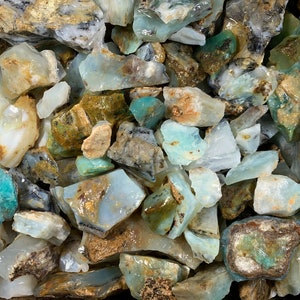 May include: A collection of rough opal stones in various shades of blue, green, and white. The stones are irregular in shape and have a natural, unpolished finish.