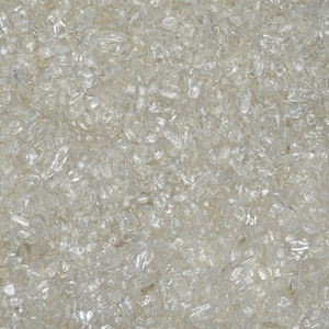 May include: A close-up view of a large quantity of small, clear quartz crystals. The crystals are scattered randomly and appear to be tumbled, giving them a smooth, rounded shape.