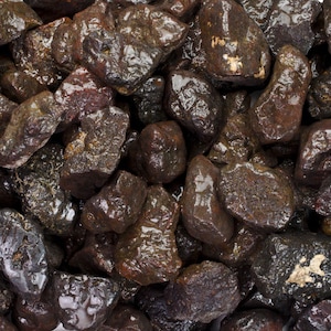 Puede incluir: Primer plano de un montón de piedras de color marrón oscuro, húmedas y de forma irregular. Las piedras tienen un tono ligeramente rojizo y un acabado brillante.