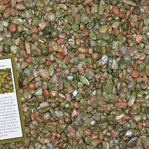 May include: A close-up image of a pile of small, smooth, polished green and red Unakite stones. The stones are tumbled and have a variety of shapes and sizes. The image also includes a small card with the text "Unakite Home Decor Healing Stones" and a description of the stone's properties.