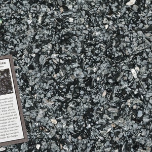 May include: A close-up view of a collection of snowflake obsidian stones, with a mix of black and gray colors. A small card with the text "Snowflake Obsidian" is visible, along with a description of the stones.