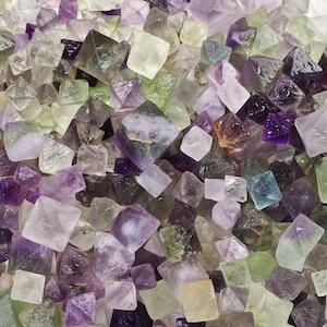 May include: A collection of small, faceted fluorite crystals in shades of green, purple, and clear. The crystals are all octahedral in shape and have a glassy luster.
