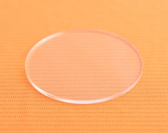 May include: A clear round glass coaster on an orange textured surface.