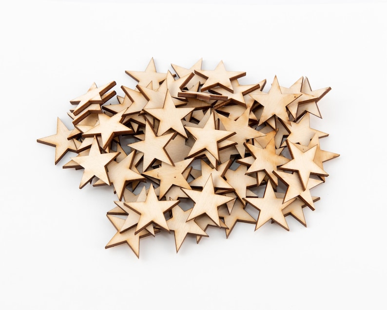Puede incluir: Un mont&oacute;n de peque&ntilde;os recortes de madera en forma de estrella. Las estrellas son de color marr&oacute;n claro con un borde marr&oacute;n m&aacute;s oscuro y est&aacute;n esparcidas sobre un fondo blanco. Estos suministros de artesan&iacute;a son ideales para proyectos de bricolaje y decoraciones.