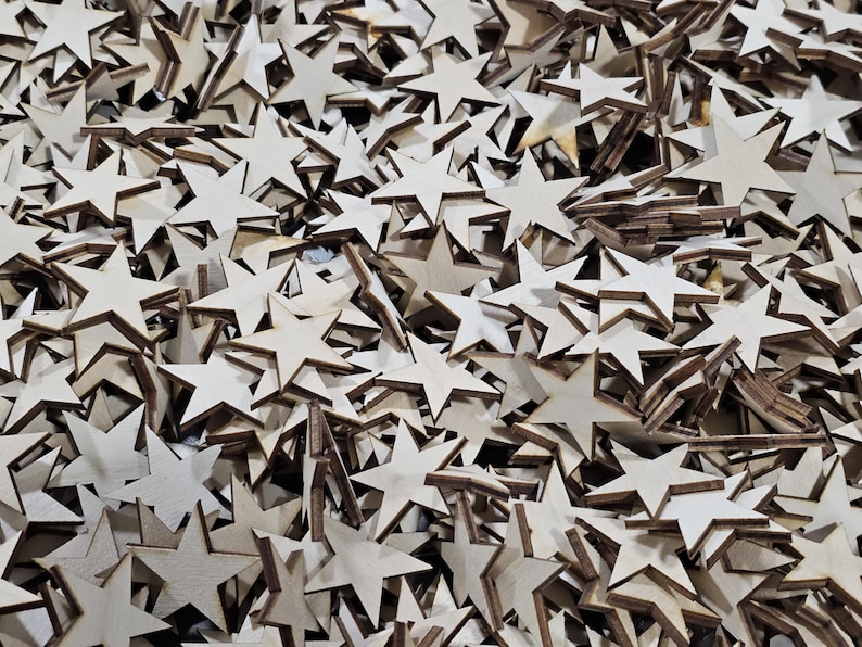 Puede incluir: Un mont&oacute;n de estrellas de madera sin terminar. Las estrellas son de color claro con un contorno marr&oacute;n m&aacute;s oscuro y var&iacute;an en tama&ntilde;o. Algunas est&aacute;n apiladas, creando una superficie texturizada. Ideal para manualidades y proyectos de bricolaje.