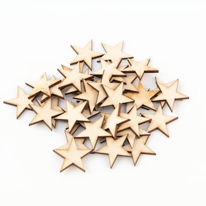 Puede incluir: Un conjunto de peque&ntilde;as estrellas de madera recortadas. Las estrellas tienen un color de madera natural con bordes marrones oscuros. Est&aacute;n dispersas sobre una superficie blanca, ideales para manualidades o decoraci&oacute;n.