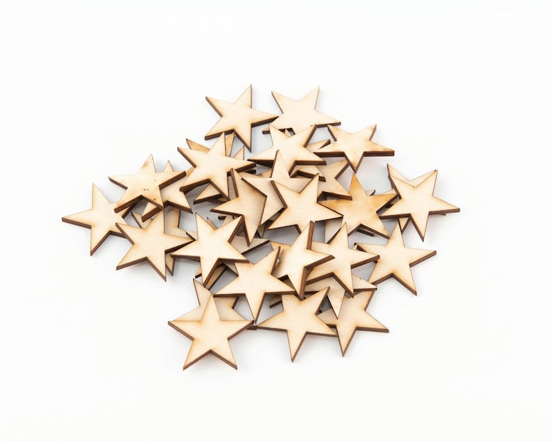 Puede incluir: Un conjunto de peque&ntilde;as estrellas de madera recortadas. Las estrellas tienen un color de madera natural con bordes marrones oscuros. Est&aacute;n dispersas sobre una superficie blanca, ideales para manualidades o decoraci&oacute;n.