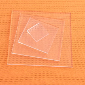 May include: Four clear acrylic squares stacked on top of each other on an orange textured background.