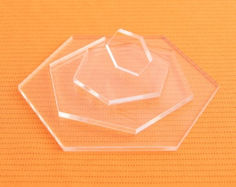 May include: Four clear acrylic hexagonal coasters of different sizes stacked on top of each other on an orange textured surface.