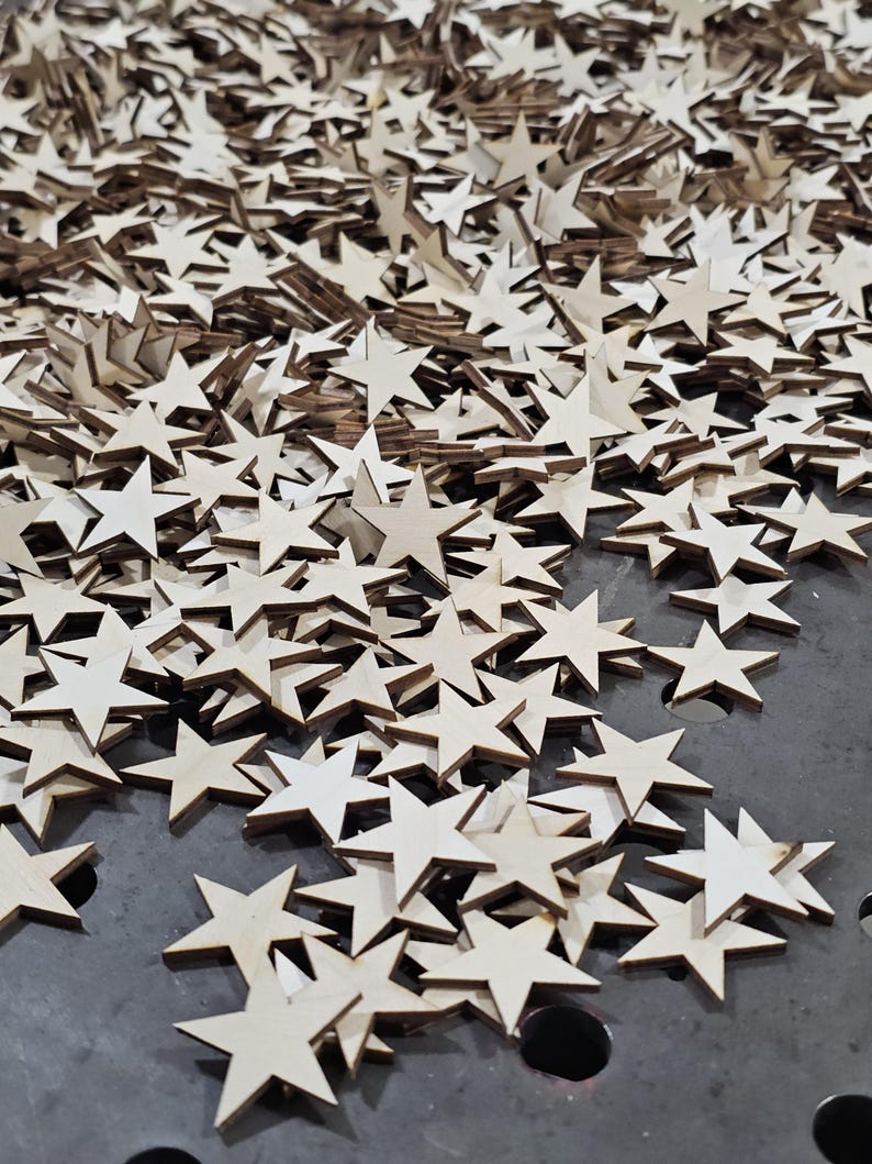 Puede incluir: Una gran colecci&oacute;n de peque&ntilde;as estrellas de madera sin terminar. Las estrellas est&aacute;n esparcidas sobre una superficie oscura, con diferentes tonos de marr&oacute;n claro y beige. La imagen est&aacute; tomada desde un &aacute;ngulo ligeramente elevado, mostrando la densidad de las estrellas.