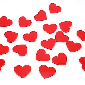 May include: A collection of glossy, red heart-shaped embellishments scattered on a white surface. These small, decorative hearts are ideal for crafts, scrapbooking, or Valentine's Day projects. The hearts are approximately 1 inch in size.
