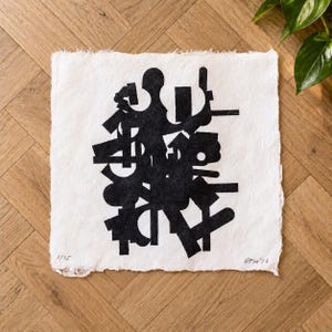 May include: A square piece of white handmade paper with deckled edges featuring a black ink abstract print composed of various geometric shapes and lines. The print is signed and numbered 1/25 in the bottom corners in graphite pencil.