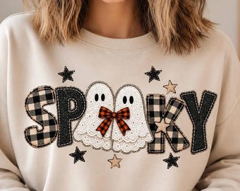May include: A beige crewneck sweatshirt featuring the text SPOOKY in a mix of black and white buffalo plaid and black glitter textures. Two white lace ghosts with a red and black plaid bow are positioned between the letters, surrounded by stars.