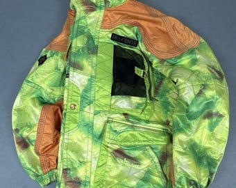 May include: A Descente hooded jacket featuring a vibrant green and yellow abstract pattern with solid orange textured shoulder and sleeve panels. The jacket includes a black chest patch, a zippered pocket, and a large front cargo pocket.