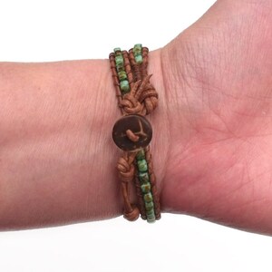 May include: A brown leather wrap bracelet with turquoise beads and a wooden button closure. The bracelet is wrapped around a wrist, showcasing its layered design and natural materials. The bracelet is approximately 7 inches in length.
