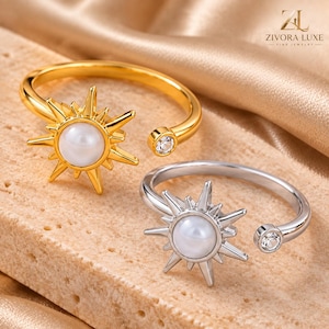 May include: Two open-style rings, one gold-toned and one silver-toned, each featuring a central white pearl surrounded by radiating sunburst rays and a single small clear stone at the opposite end of the band, branded with ZIVORA LUXE text.