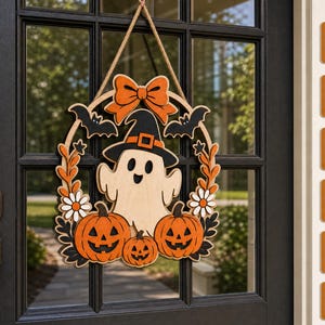Puede incluir: Un colgador de puerta de madera para Halloween con un fantasma central con sombrero de bruja negro, rodeado de calabazas naranjas, murciélagos negros, flores blancas y un lazo naranja, suspendido por una cuerda. A la derecha, formatos SVG, DXF, EPS, AI, PDF, DWG.