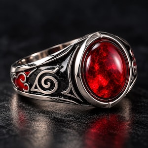 May include: A silver-toned metal ring featuring a large, oval-shaped, faceted red gemstone in the center. The band is decorated with black enamel detailing, including a spiral symbol and red cloud-like shapes engraved along the sides.