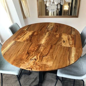 May include: A round wooden dining table with a natural wood grain pattern. The table has a dark brown finish and is made of solid wood. The table is surrounded by four chairs.