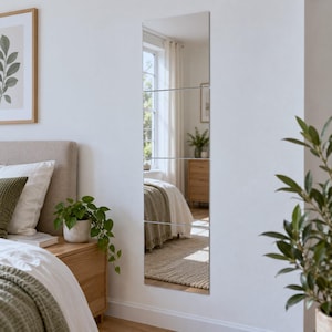 Puede incluir: Un espejo de pared alto y rectangular compuesto por cuatro paneles cuadrados individuales apilados verticalmente. El espejo presenta una superficie de cristal reflectante con finas juntas horizontales entre cada sección, montado en una pared blanca.