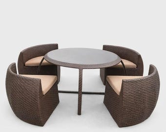 May include: A round dining table with a dark glass top and four curved chairs, all featuring a dark brown woven wicker exterior. Each chair includes a light tan seat cushion, and the chairs are designed to tuck neatly under the table frame.