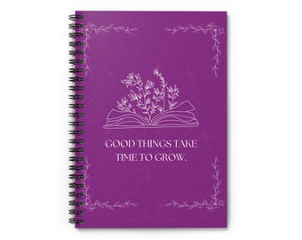 May include: A purple spiral-bound notebook featuring a white line-art illustration of an open book with flowers growing out of it. The text GOOD THINGS TAKE TIME TO GROW is printed in white in the center, surrounded by a delicate floral border.