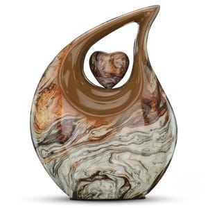 May include: A teardrop-shaped ceramic sculpture featuring a glossy brown upper arch and a heart-shaped accent suspended in the center. The lower body displays a swirling marbled pattern of white, cream, dark brown, and metallic bronze tones.
