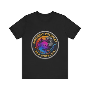 May include: A black short-sleeve t-shirt featuring a circular graphic on the chest. The design shows a gradient-colored cat wearing headphones, a modular synthesizer, and cables, with the text PATCHBAY PUSSYCAT MOD SYNTH I DIV.