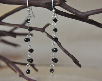 May include: A pair of long silver dangle earrings with black beads. The earrings are hanging from a branch.