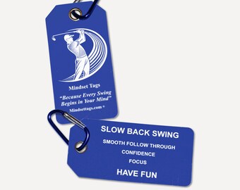 May include: Two rectangular blue luggage-style tags with metal grommets and dark blue carabiners. One tag features a white graphic of a golfer and the text Mindset Tags Because Every Swing Begins in Your Mind. The other lists golf tips.