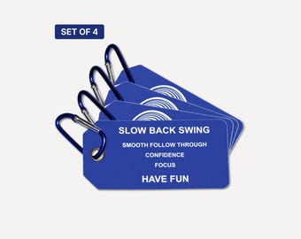 May include: A set of four blue rectangular tags with silver metal carabiners. Each tag features white text reading: SLOW BACK SWING, SMOOTH FOLLOW THROUGH, CONFIDENCE, FOCUS, HAVE FUN. A small graphic of a circular pattern is visible at the top.